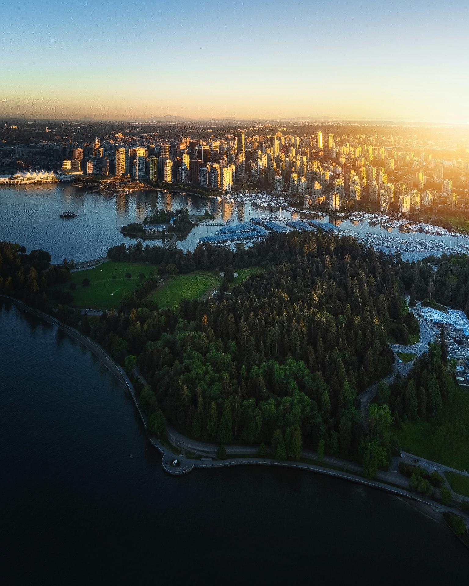 Aerial sunset view of a coastal city skyline with forested parkland and marina